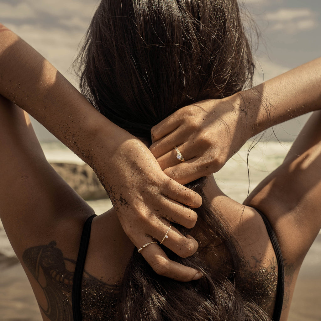 A woman holding hair back at the beach wearing Scéona sustainable jewellery
