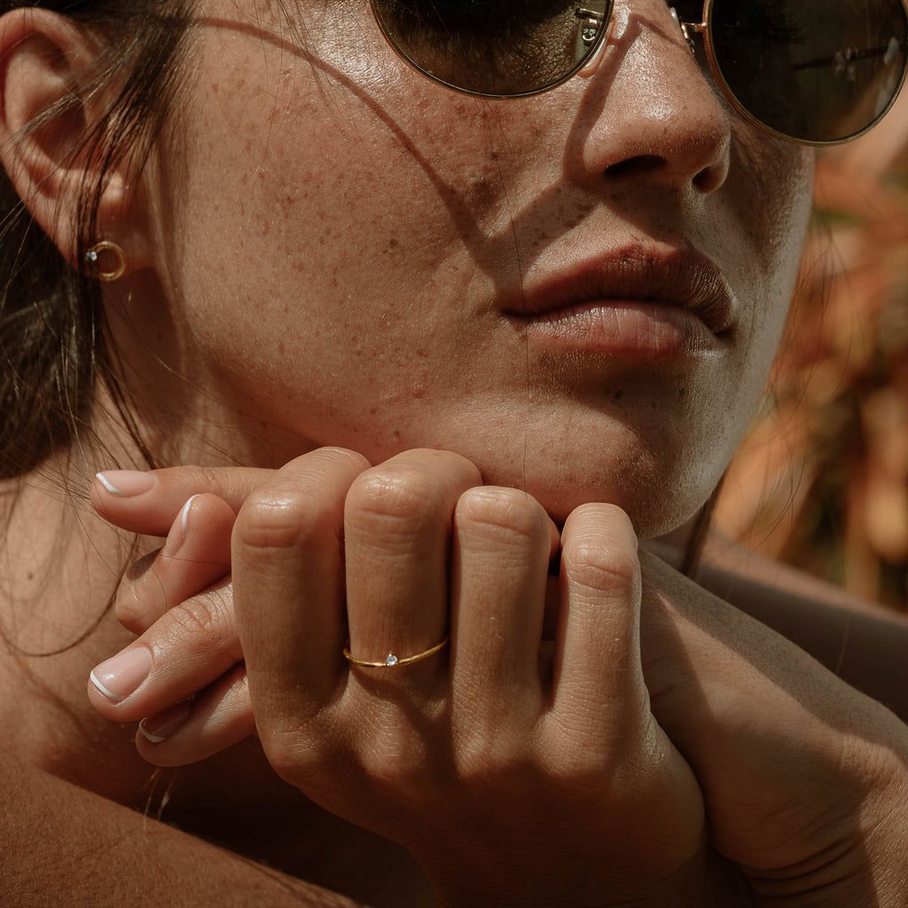 A woman wearing sunglasses, Scéona minimalist gold ring Ili, and Scéona gold studs earrings Jumna